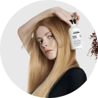 A bottle of L’Oréal hair product being held up against long blonde hair.