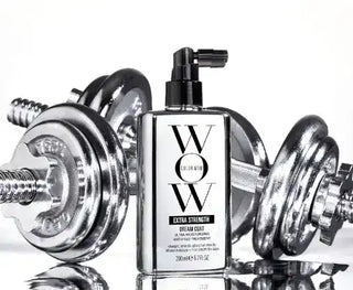 Black and white bottle of Color WOW Dream Coat hair product positioned between chrome dumbbells.