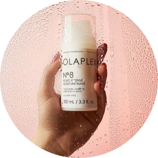 A bottle of Olaplex No. 8 Bond Intense Moisture Mask being held up against water droplets.