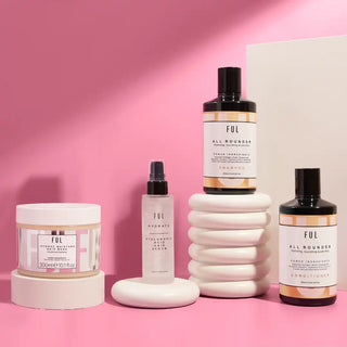 Collection of skincare products displayed on white ceramic stands against a pink backdrop.