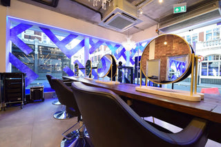 Curved wooden salon counter with mounted circular mirrors and black styling chairs.