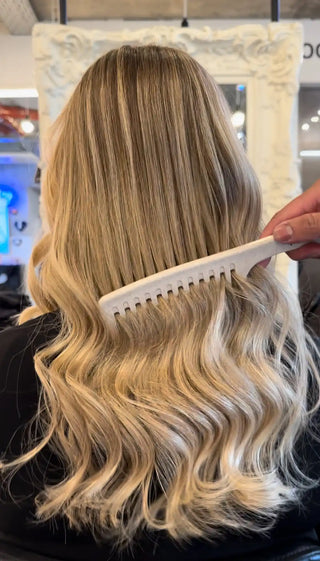 Long wavy blonde hair being combed with a wide-toothed comb.