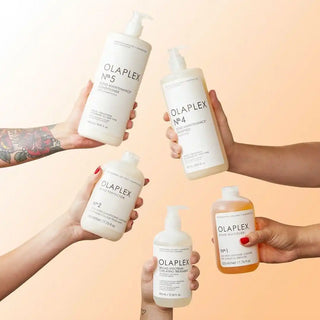 Multiple bottles of Olaplex hair care products being held by different hands.