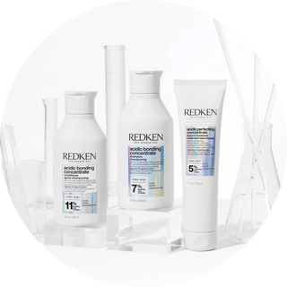 Three white Redken hair care product bottles with blue labeling.