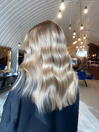 Wavy blonde hair styled in soft, glossy waves falls just past shoulder length.